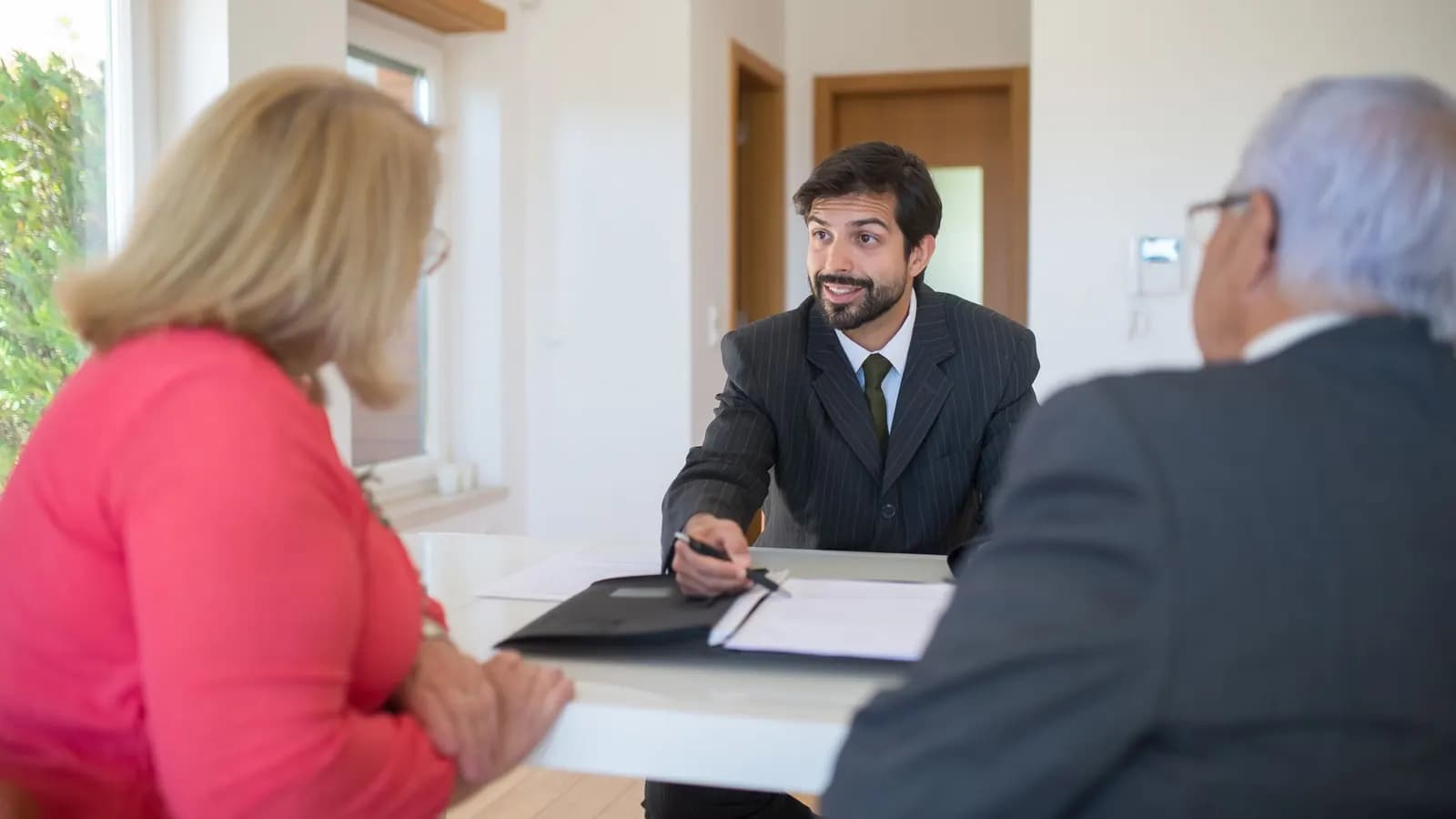 An advisor in a pinstripe suit reviews documents with an older couple across a white table.