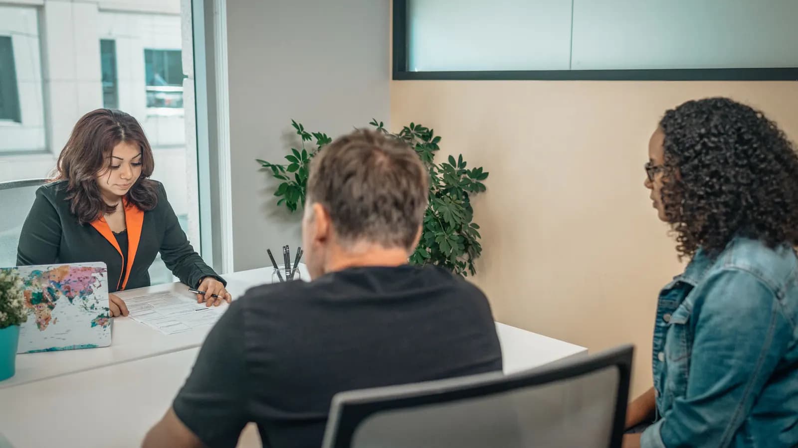 Office employee at a desk going over a printed form with two people seated across from her