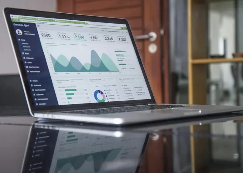 Laptop on a reflective desk showing an analytics dashboard with area charts and metric tiles