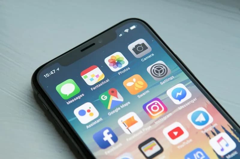 Close-up of a smartphone home screen full of app icons, resting on a light grey surface