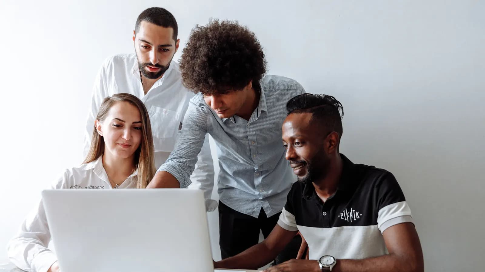 Four colleagues gather around a white laptop as one of them leans over and points at the screen