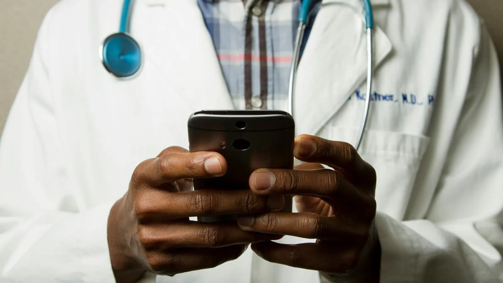 Doctor in a white coat with a stethoscope around the neck, holding a smartphone in both hands