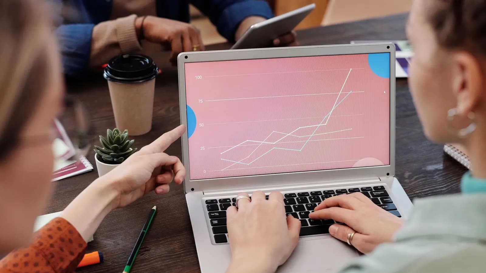 Two colleagues at a desk, one pointing at a line chart on a laptop screen
