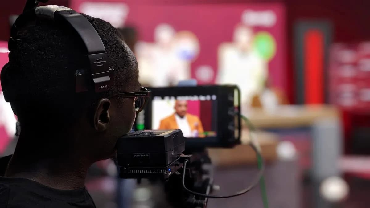 Camera operator with headphones filming a presenter in a TV studio, seen on the viewfinder