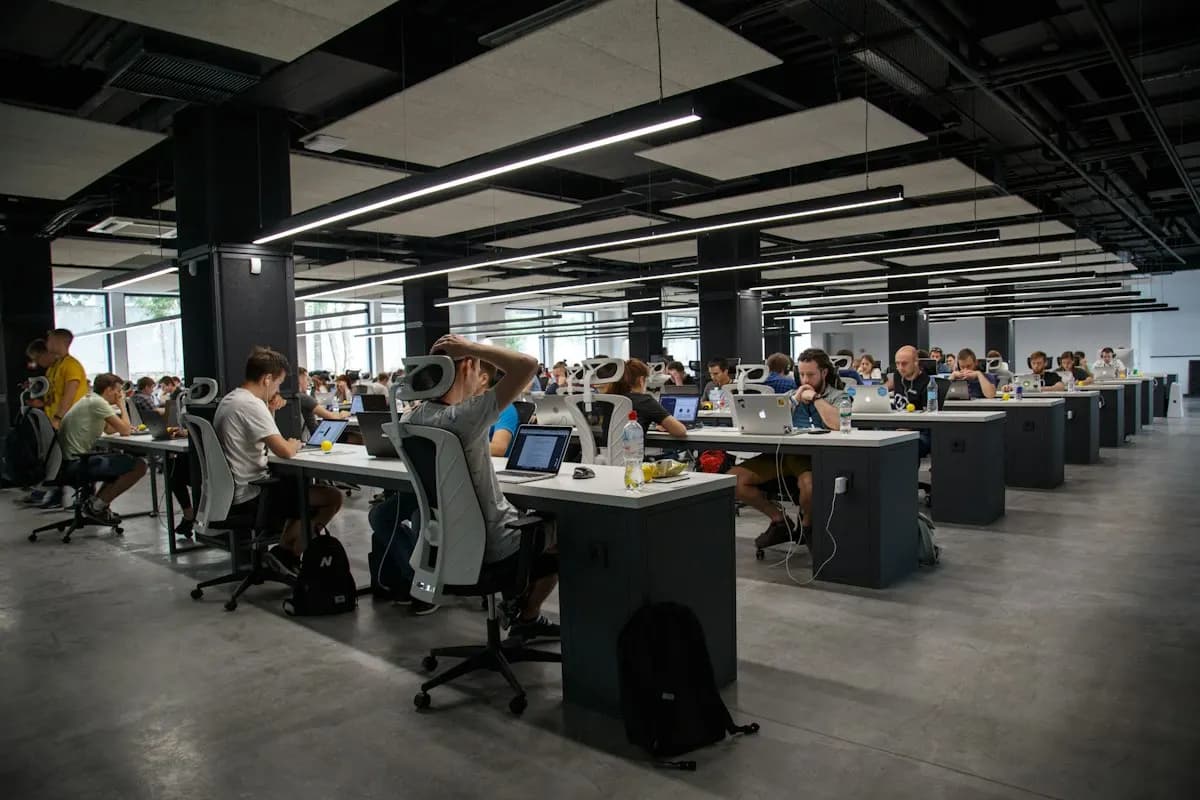 Rows of people working on laptops at long desks in a large open-plan office