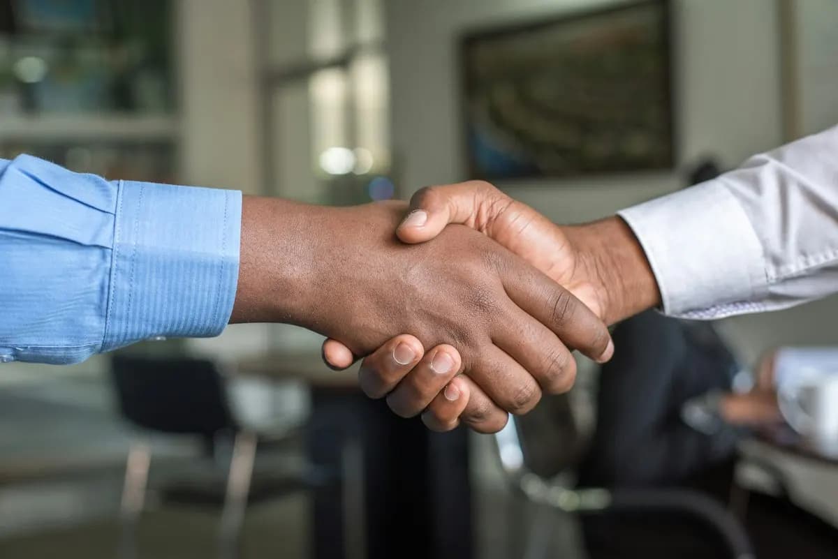 Close-up handshake between two people in blue and white shirt sleeves in an office