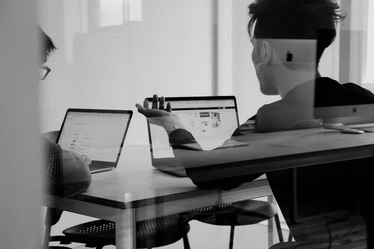 Black and white shot through glass of two people working together on laptops at a desk