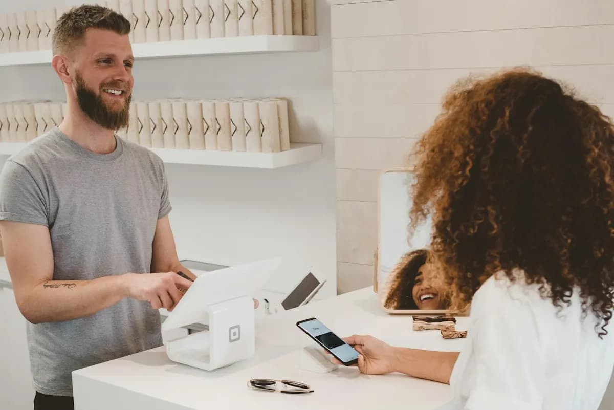 Customer holds her phone over a card reader while a smiling cashier stands at the counter