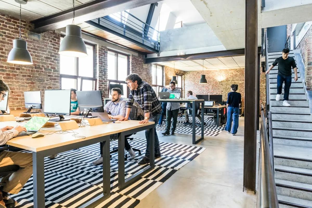 Team at work in a brick-walled loft office with desks, monitors, pendant lamps and a staircase