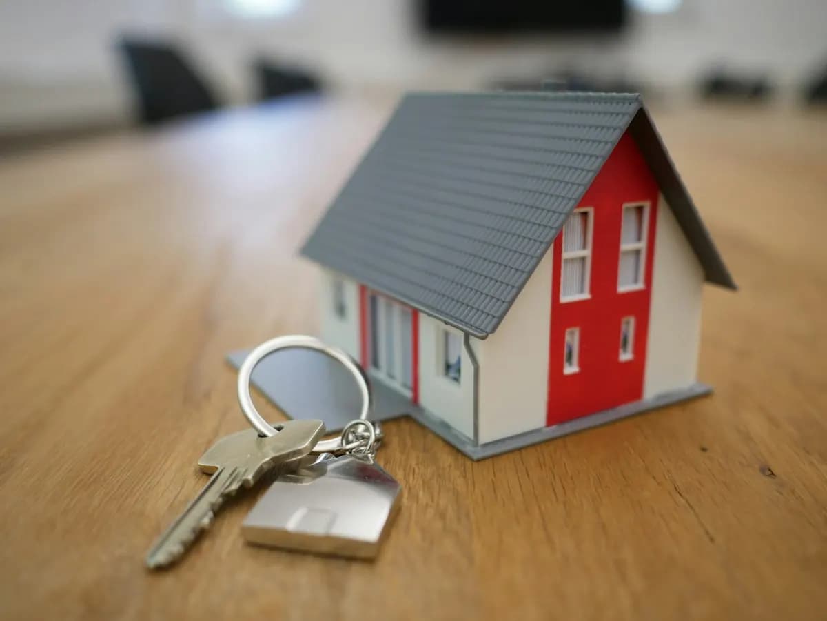 Miniature house model next to a key on a house-shaped keyring, resting on a wooden table