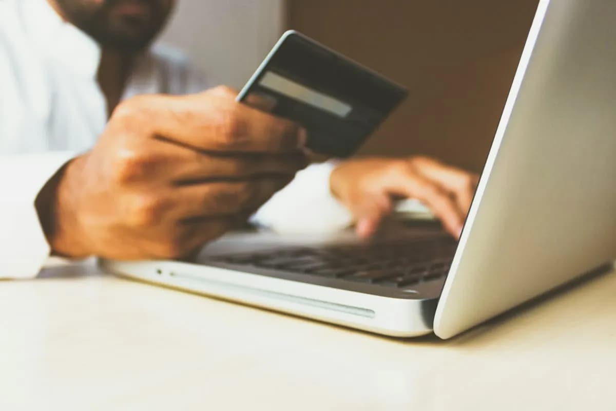 Person holding a payment card while typing on a silver laptop keyboard