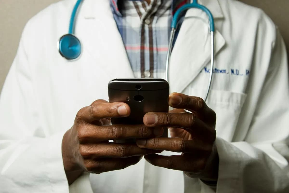 Doctor in a white coat with a stethoscope holding a smartphone in both hands