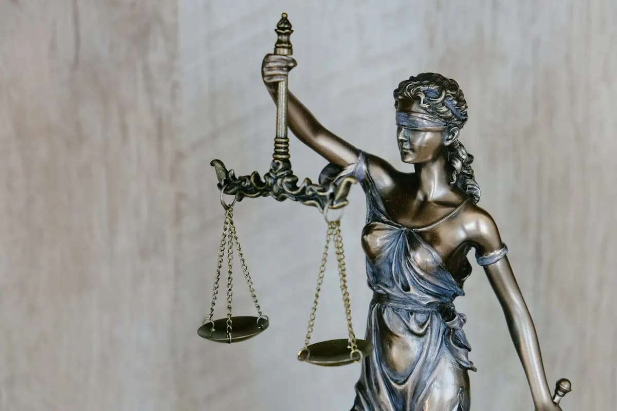 Bronze statue of blindfolded Lady Justice holding balance scales against a pale wooden wall