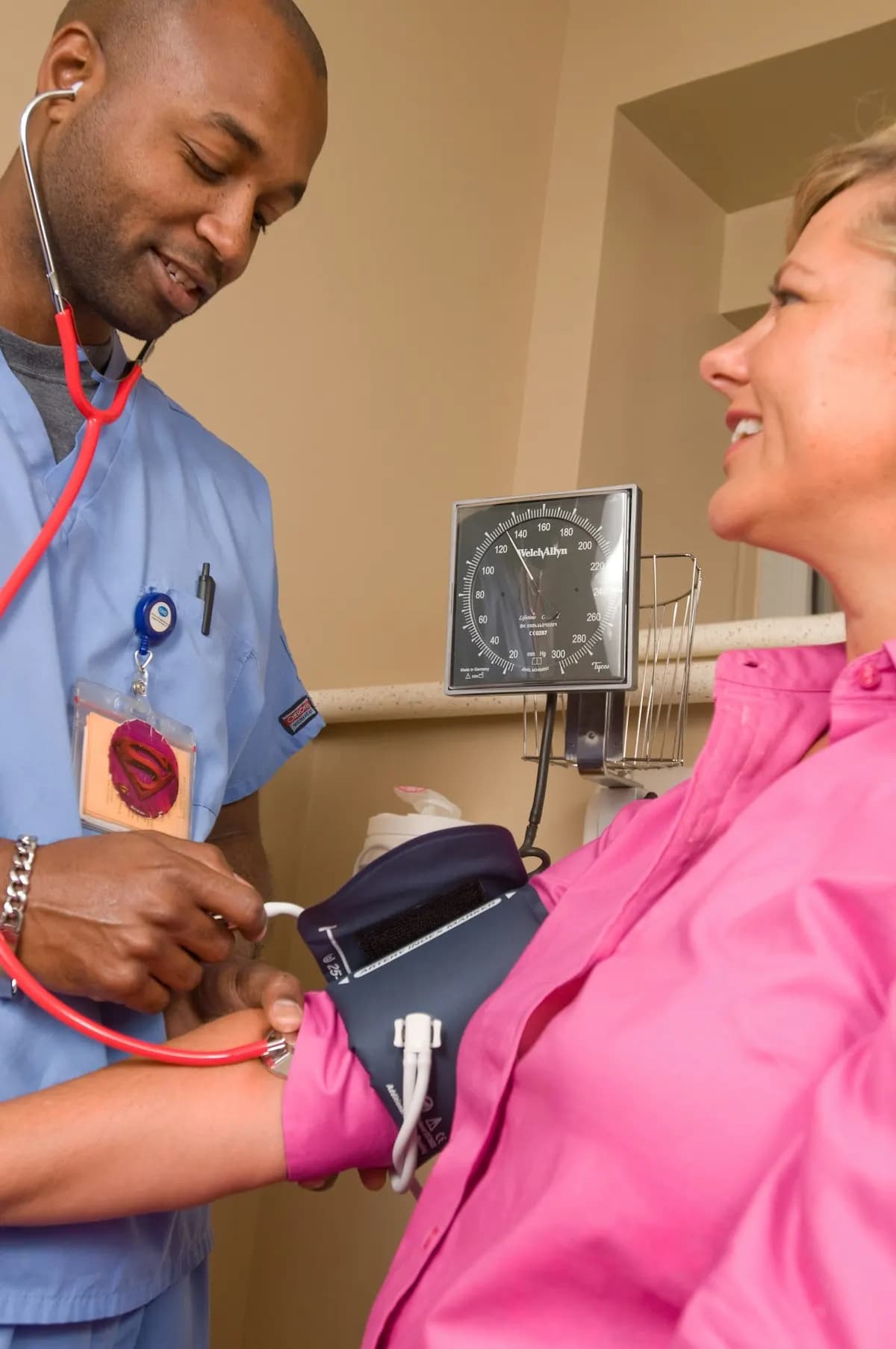 Clinician in blue scrubs taking a smiling woman's blood pressure with a cuff and stethoscope
